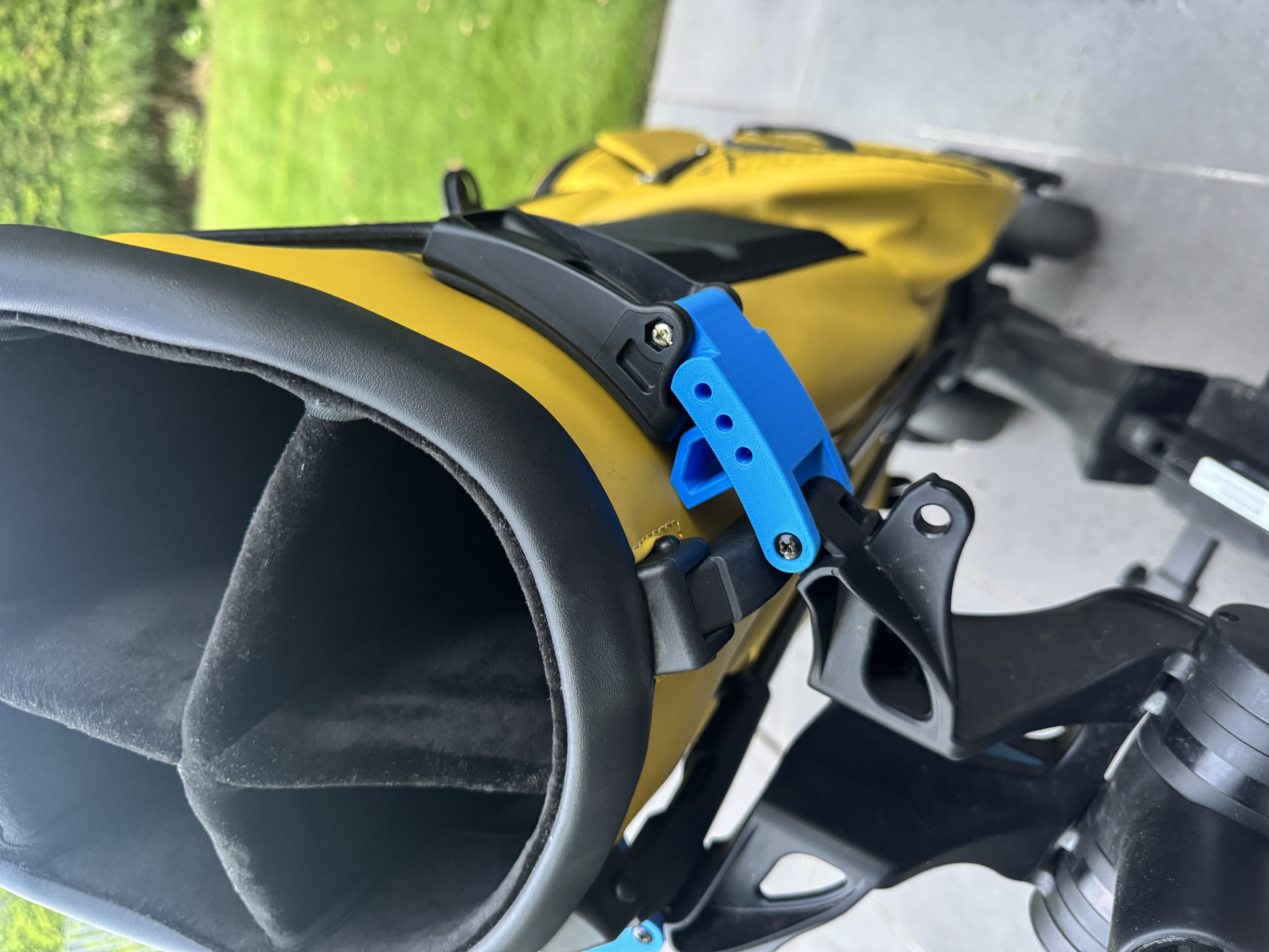 Close-up of the blue 3D-printed clip attaching a yellow golf bag securely to the MGI trolley frame